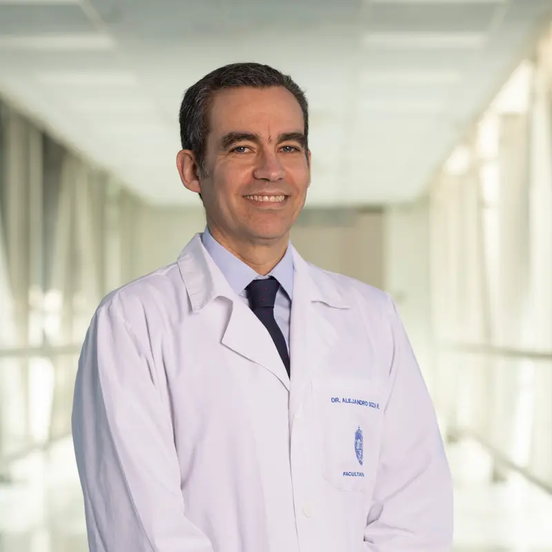 El Dr. Alejandro Soza con bata blanca, de pie en un pasillo de vidrio.